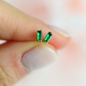 May include: A pair of gold earrings with emerald green baguette-shaped gemstones.