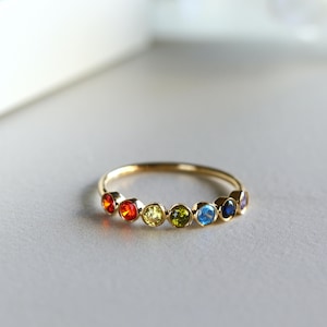 May include: A gold band ring with seven colorful gemstones set in a rainbow pattern. The gemstones are red, orange, yellow, green, blue, light blue, and purple.