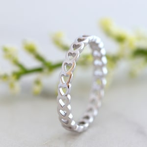 May include: A silver ring featuring a heart-shaped design. The ring is crafted from a thin band of metal with a series of interconnected hearts.