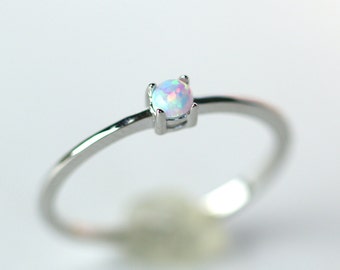May include: A delicate silver ring with a small, round opal gemstone. The opal has a white base with iridescent pink and blue hues.