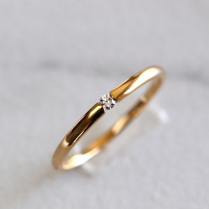 May include: A simple gold band ring with a single small diamond set in the center.