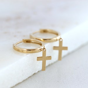 May include: Gold hoop earrings with a small cross charm hanging from each hoop. The earrings are marked "JL 10K" on the back of the hoop.
