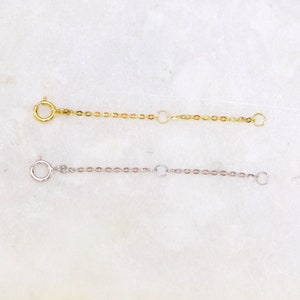 May include: Two gold and silver chain extenders with lobster clasps. The extenders are on a white background.