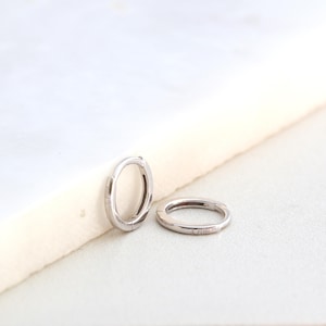 May include: Two silver hoop earrings on a white surface. The earrings are small and simple, with a smooth finish.
