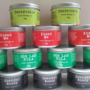 Puede incluir: Una colecci&oacute;n de 10 tarros de velas con varios aromas y nombres. Los tarros son plateados con etiquetas negras, verdes y rojas. Las etiquetas tienen nombres como "Knead Me", "Ooh Lah Hula" y "Scandal Woody". Cada tarro contiene 60 gramos de aceite de masaje para velas.