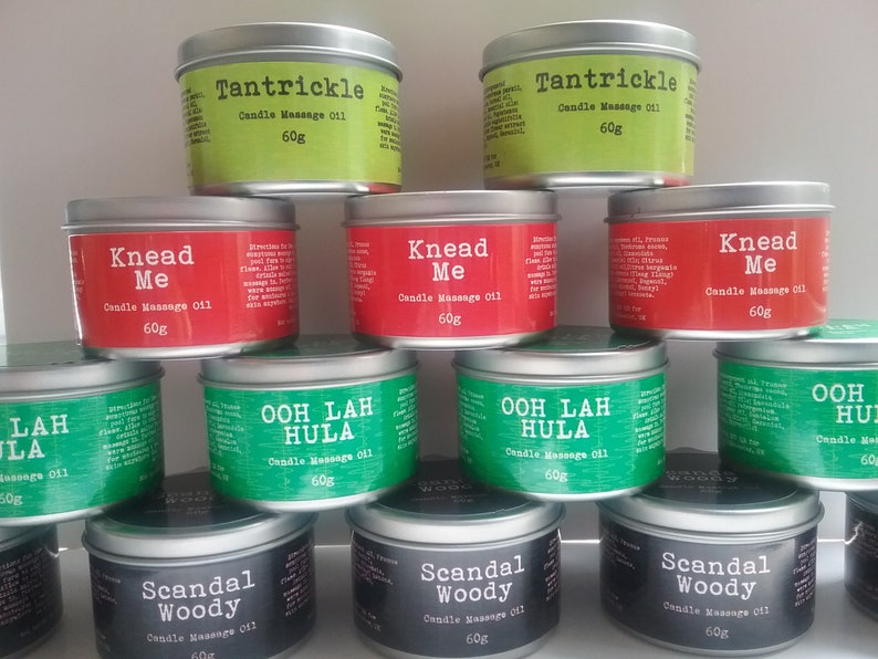 Puede incluir: Una colecci&oacute;n de 10 tarros de velas con varios aromas y nombres. Los tarros son plateados con etiquetas negras, verdes y rojas. Las etiquetas tienen nombres como "Knead Me", "Ooh Lah Hula" y "Scandal Woody". Cada tarro contiene 60 gramos de aceite de masaje para velas.