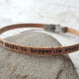 May include: Cork bracelet with a silver clasp and the inscription "It's a shift to happen in every area".