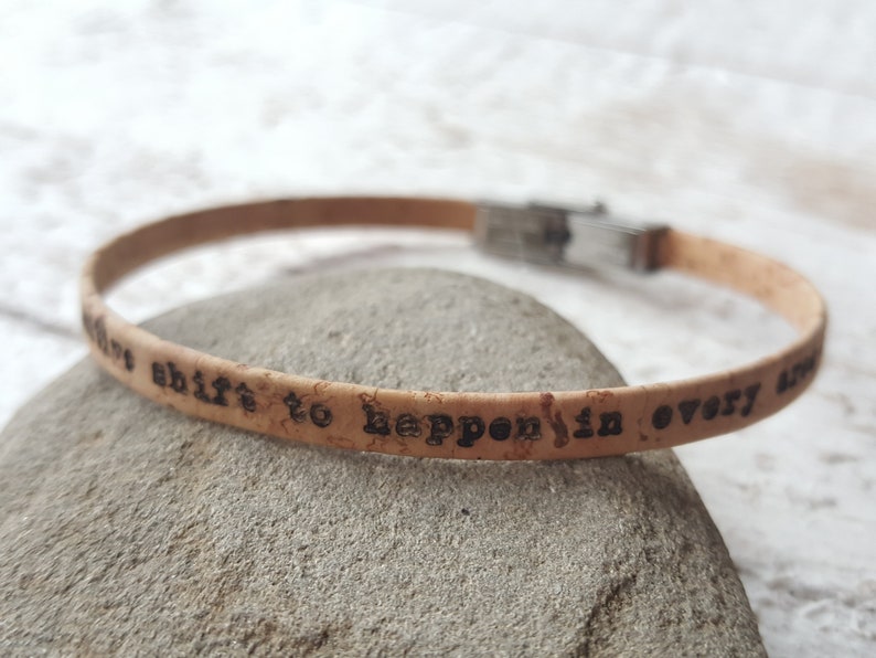 May include: Cork bracelet with a silver clasp and the inscription "It's a shift to happen in every area".
