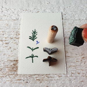 May include: Four wooden stamps with different designs. The stamps are on a white card. The designs include a sprig of leaves, a flower, a bird, and a leaf.
