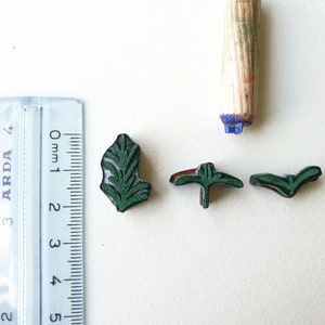 May include: Four green rubber stamps with leaf designs. The stamps are approximately 1 cm in size. A wooden roller stamp is also visible in the image.