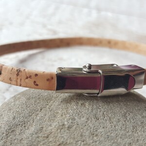 May include: A light brown cork bracelet with a silver clasp. The bracelet has the words "my life" engraved on it.
