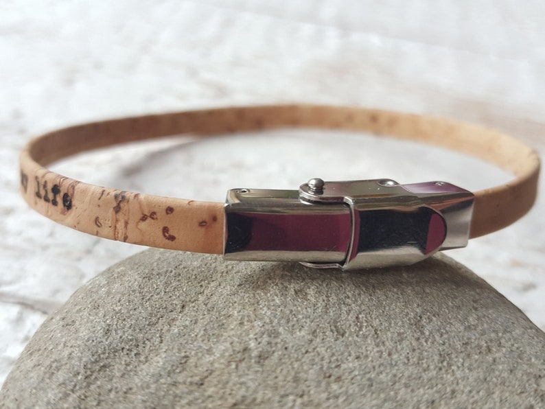 May include: A light brown cork bracelet with a silver clasp. The bracelet has the words "my life" engraved on it.