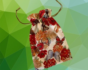 Pode incluir: Uma bolsa de cordão branco com uma estampa floral com flores vermelhas, laranja e amarelas e borboletas. A bolsa tem um fundo verde e branco.