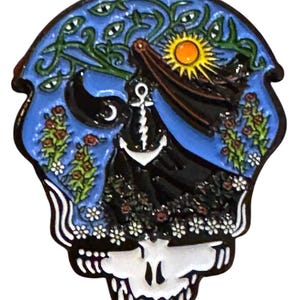 May include: A black and white enamel pin featuring a skull with a blue, black, and white design. The skull has a floral pattern around the bottom and a sun with a yellow face and orange rays in the top center. The design includes a black figure with a white ankh symbol and a white anchor.