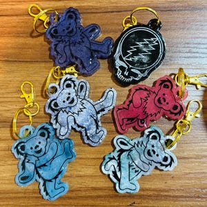 May include: Six colorful keychains featuring a Grateful Dead theme.  The keychains include a black and white skull with lightning bolt, a blue bear, a red bear, a light blue bear, a teal bear, and a purple bear.