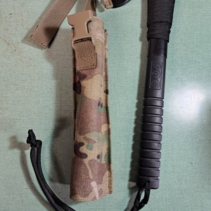 May include: A black tactical tomahawk with a black paracord wrapped handle and a camo sheath with a black strap and buckle. The handle has the word "DOS" printed on it.