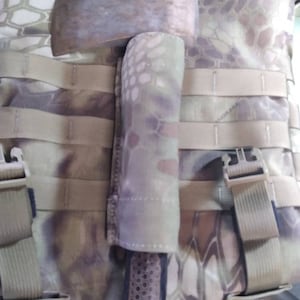 May include: A camouflage-patterned tactical bag with a brown axe secured to the front. The axe has a black handle and a brown leather sheath.