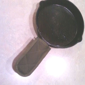 May include: A black cast iron skillet with a dark gray fabric pot holder.