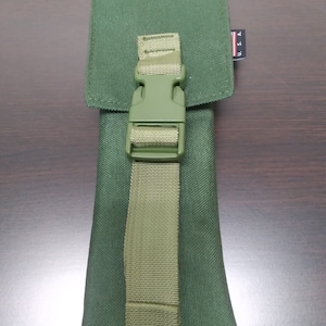 May include: A green canvas pouch with a flap closure and a buckle strap. The pouch has a rectangular shape and a textured surface. The strap is olive green and secures the flap. A small tag reads "U.S.A."