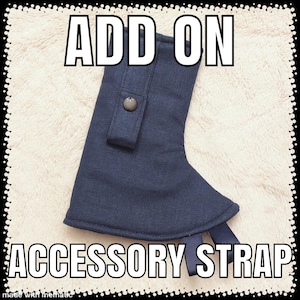 May include: A navy blue accessory strap with the words "ADD ON" and "ACCESSORY STRAP" in white block letters. The strap has a button closure and two navy blue ribbon straps. The background is a light, textured fabric.