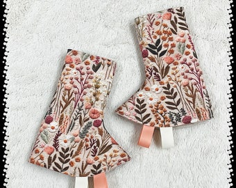 May include: Two beige fabric boot cuffs with a floral pattern in shades of pink, brown, and green. The cuffs have white and pink ribbon ties.