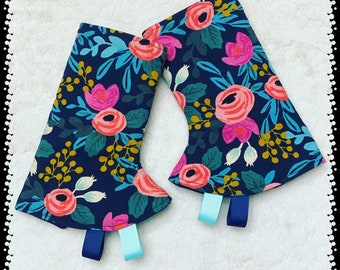 May include: A pair of blue fabric pot holders with a floral pattern in shades of pink, green, and yellow. The pot holders have blue and turquoise ribbon ties.