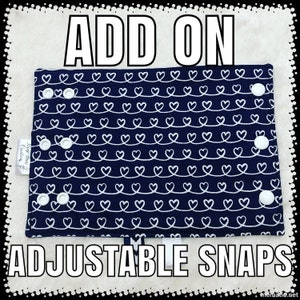 May include: Add-on adjustable snaps for a baby carrier or other fabric project. The snaps are white and are attached to a blue fabric with a white heart pattern. The fabric has the text "Just You & Me Creations" printed on it.