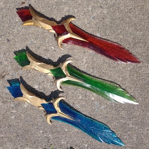 Puede incluir: Tres dagas decorativas con mangos dorados y hojas de vidrio rojo, verde y azul.