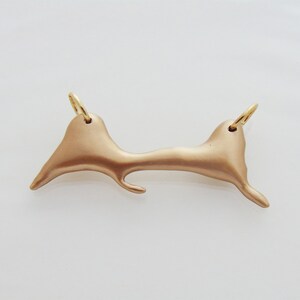 Può includere: Un ciondolo dorato a forma di isola. Il ciondolo ha due anelli a salto per attaccare una catena.