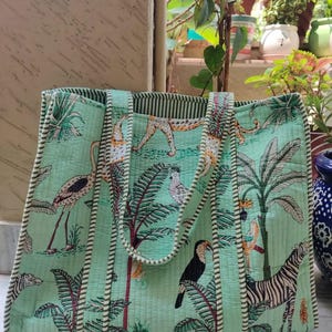 May include: A green quilted tote bag with a jungle print featuring zebras, toucans, flamingos, and leopards. The bag has white and green striped handles.