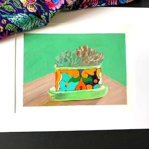 May include: A colorful painting of a succulent plant in a patterned pot. The pot is orange with blue, green, and yellow floral designs. The plant sits on a green saucer against a green background. A colorful textile is in the background.