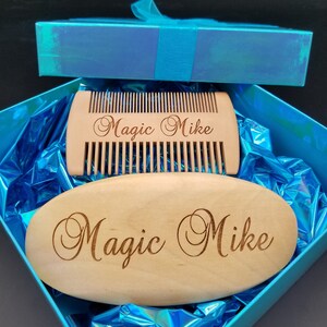 May include: A wooden beard comb and oval-shaped brush set, both engraved with "Magic Mike", presented in a blue gift box with a matching ribbon. The comb has fine teeth, and the brush is smooth. The set is nestled on shiny blue wrapping.