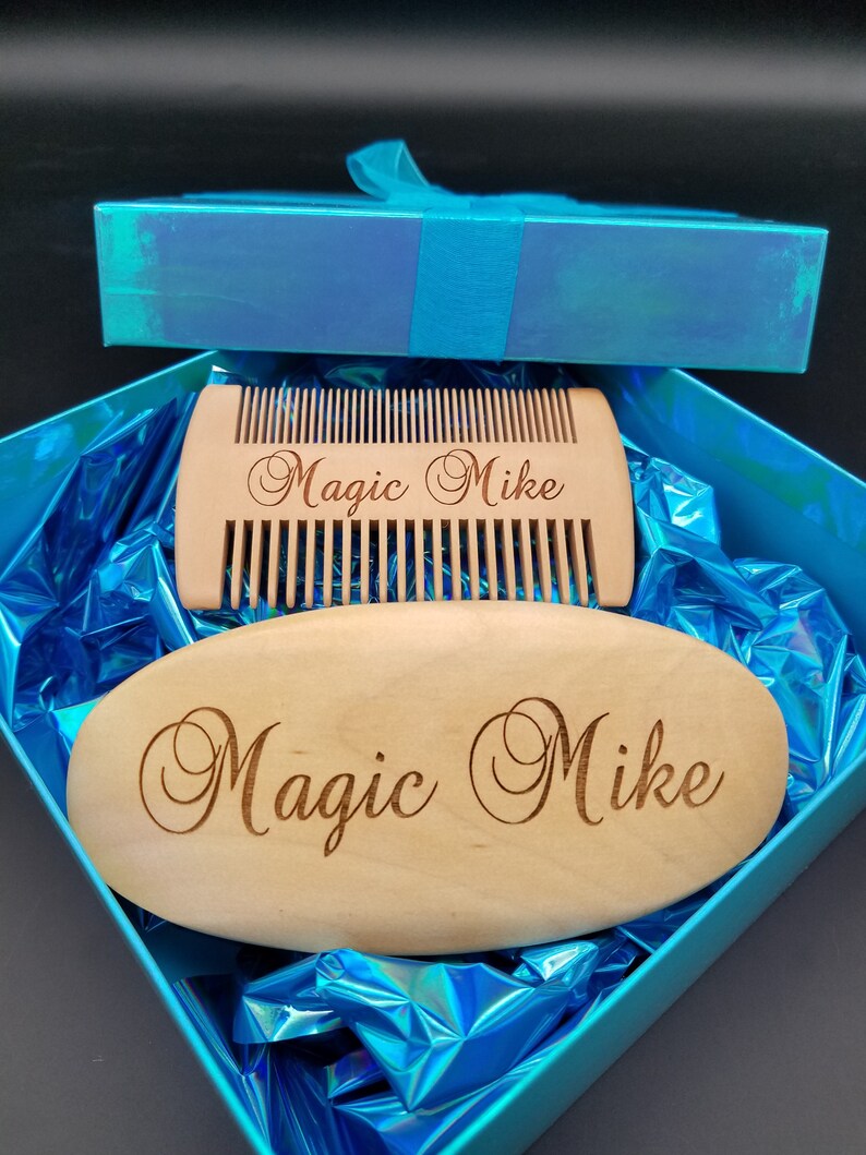May include: A wooden beard comb and oval-shaped brush set, both engraved with "Magic Mike", presented in a blue gift box with a matching ribbon. The comb has fine teeth, and the brush is smooth. The set is nestled on shiny blue wrapping.