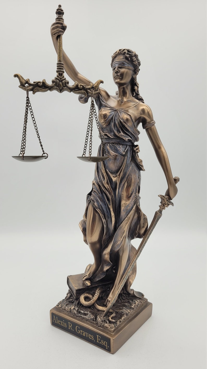 May include: Bronze statue of the blindfolded figure of Justice holding a sword and scales. The statue is standing on a book with a snake wrapped around it. The base of the statue has the inscription "Alexis R. Graves, Esq."