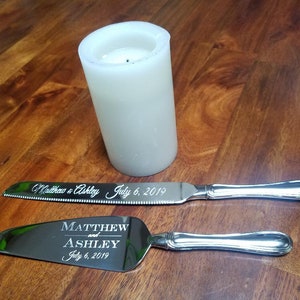 May include: A silver cake knife and server set with engraved text "Matthew and Ashley July 6, 2019".