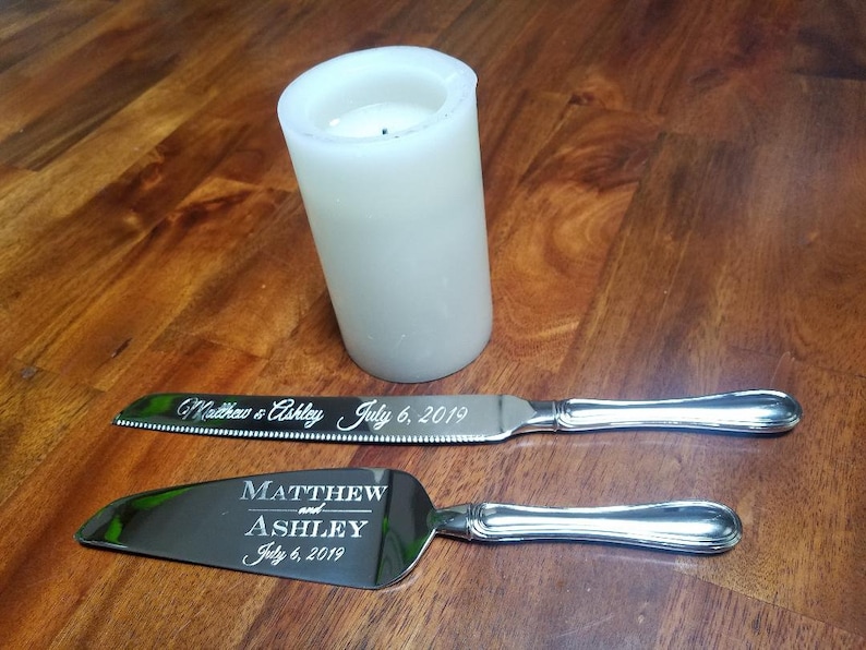 May include: A silver cake knife and server set with engraved text "Matthew and Ashley July 6, 2019".