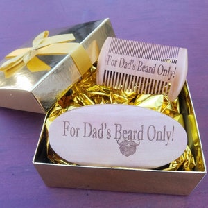 May include: A gold gift box with a yellow ribbon contains a wooden beard comb and a wooden beard brush. The comb and brush are engraved with the text "For Dad's Beard Only!" and a beard graphic. The box is lined with gold tissue paper.