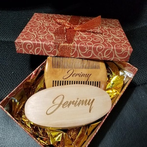 May include: A gift box with a red and gold patterned exterior, tied with a shimmering orange ribbon. Inside, a wooden comb and oval brush, both engraved with the name "Jerimy", rest on gold foil.