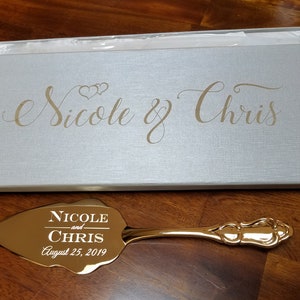May include: Gold cake server with a leaf-shaped blade engraved with "Nicole and Chris August 25, 2019". The server comes in a white box with the names "Nicole & Chris" engraved in gold.