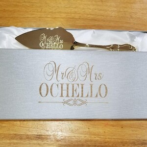 May include: Gold cake server in a gray box with the text "Mr. & Mrs. Ochello" engraved on the box and the server.