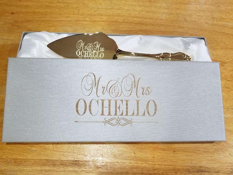 May include: Gold cake server in a gray box with the text "Mr. & Mrs. Ochello" engraved on the box and the server.