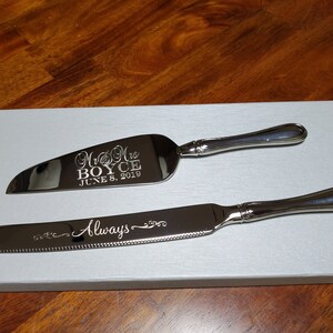 May include: A silver cake knife and server set with engraved text. The server has the text "Mr & Mrs BOYCE JUNE 8, 2019". The knife has the text "Always" engraved on it.