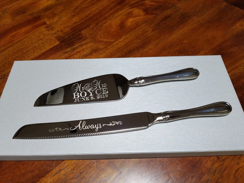 May include: A silver cake knife and server set with engraved text. The server has the text "Mr & Mrs BOYCE JUNE 8, 2019". The knife has the text "Always" engraved on it.