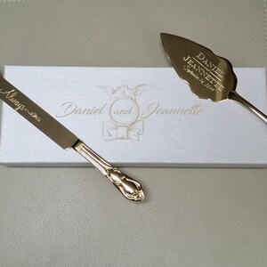 May include: Gold wedding cake knife and server set in a white box. The knife has the inscription "Always" and the server has the inscription "Daniel and Jeannette September 14, 2019".