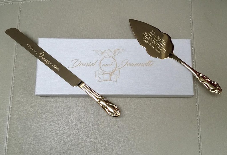 May include: Gold wedding cake knife and server set in a white box. The knife has the inscription "Always" and the server has the inscription "Daniel and Jeannette September 14, 2019".