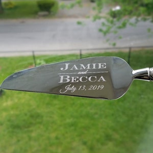 May include: Silver cake server with the text "Jamie and Becca July 13, 2019" engraved on the blade.