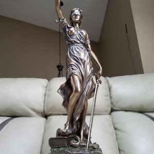 May include: Bronze statue of the figure of Justice, blindfolded, holding a sword and standing on a book with a snake. The base of the statue has a black plaque with the text "Kieffer Law Office".