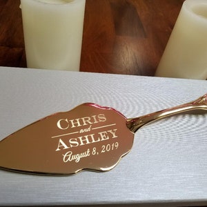 May include: Gold cake server with a decorative handle. The server is engraved with the text "CHRIS and ASHLEY August 8, 2019".