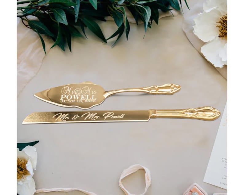 May include: Gold wedding cake knife and server set with engraved text "Mr. & Mrs. Powell June 18, 2020" and "Mr. & Mrs. Powell".