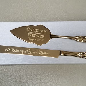 May include: Gold-toned cake knife and server set with engraved text "Cathleen and Werner May 10, 1969" on the server and "50 Wonderful Years Together" on the knife.